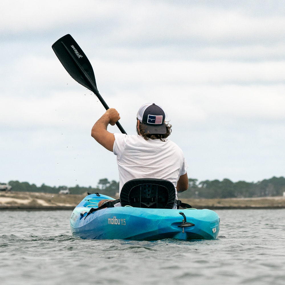 A man in a white shirt and backwards hat paddles a lone blue kayak across the Navarre intercoastal waterway