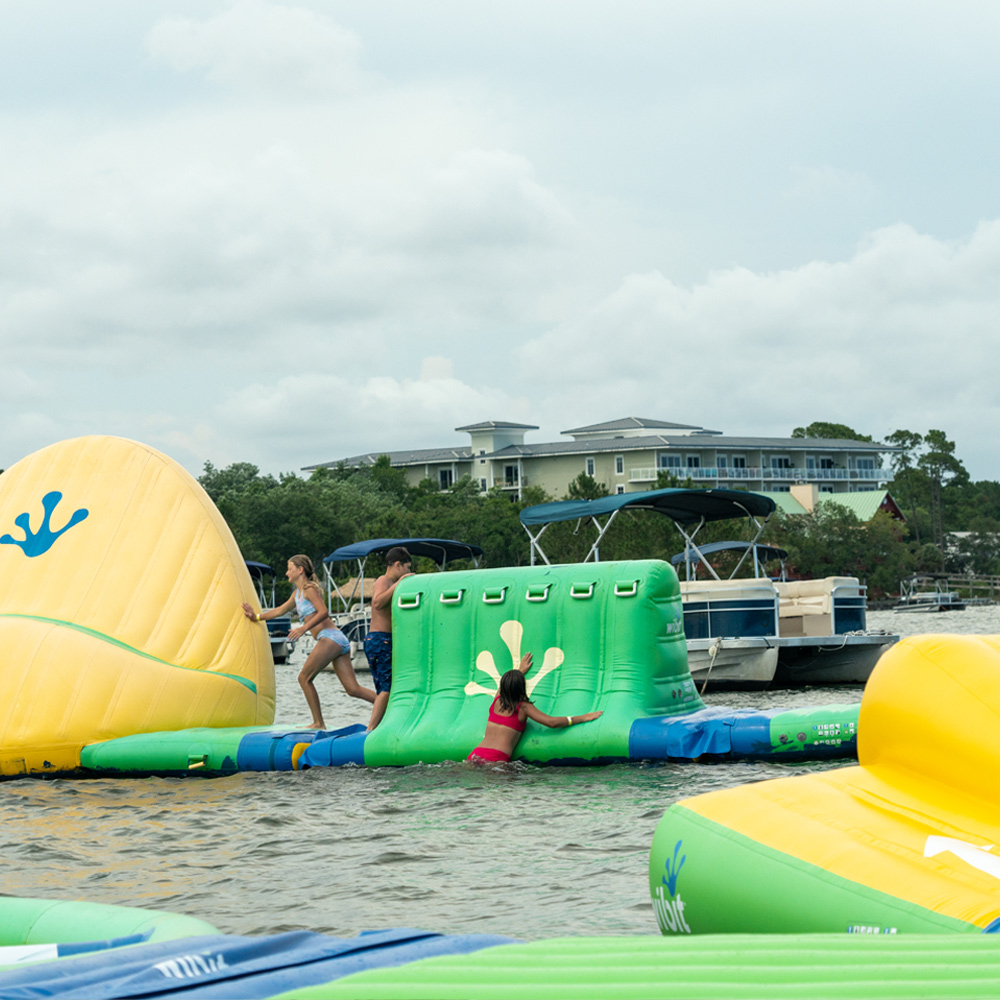 Kids playing on the yellow and green inflatable Wibit waterpark at Navarre Family Watersports