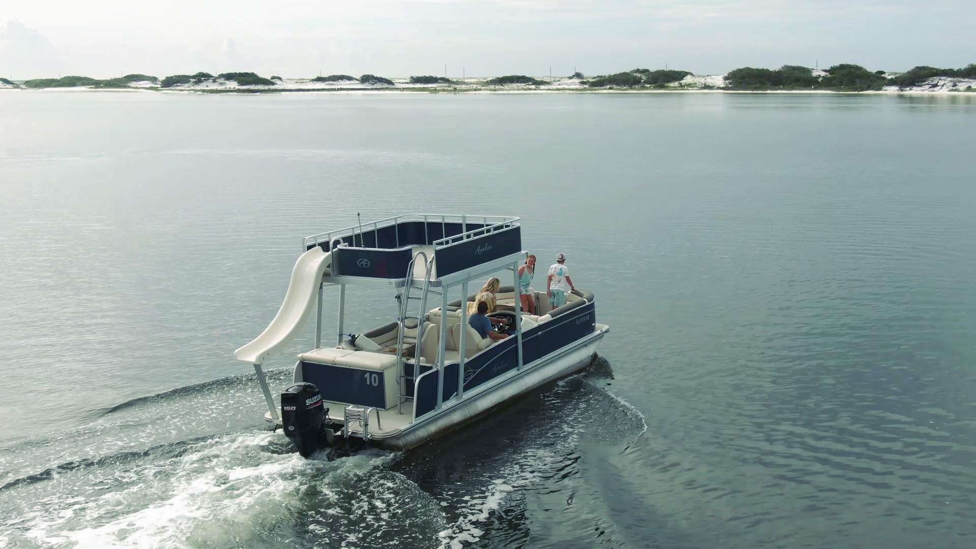 A blue Avalon double-decker Pontoon Boat with a white Slide coming off the back idles across the glassy water of Navarre's intercoastal waterway